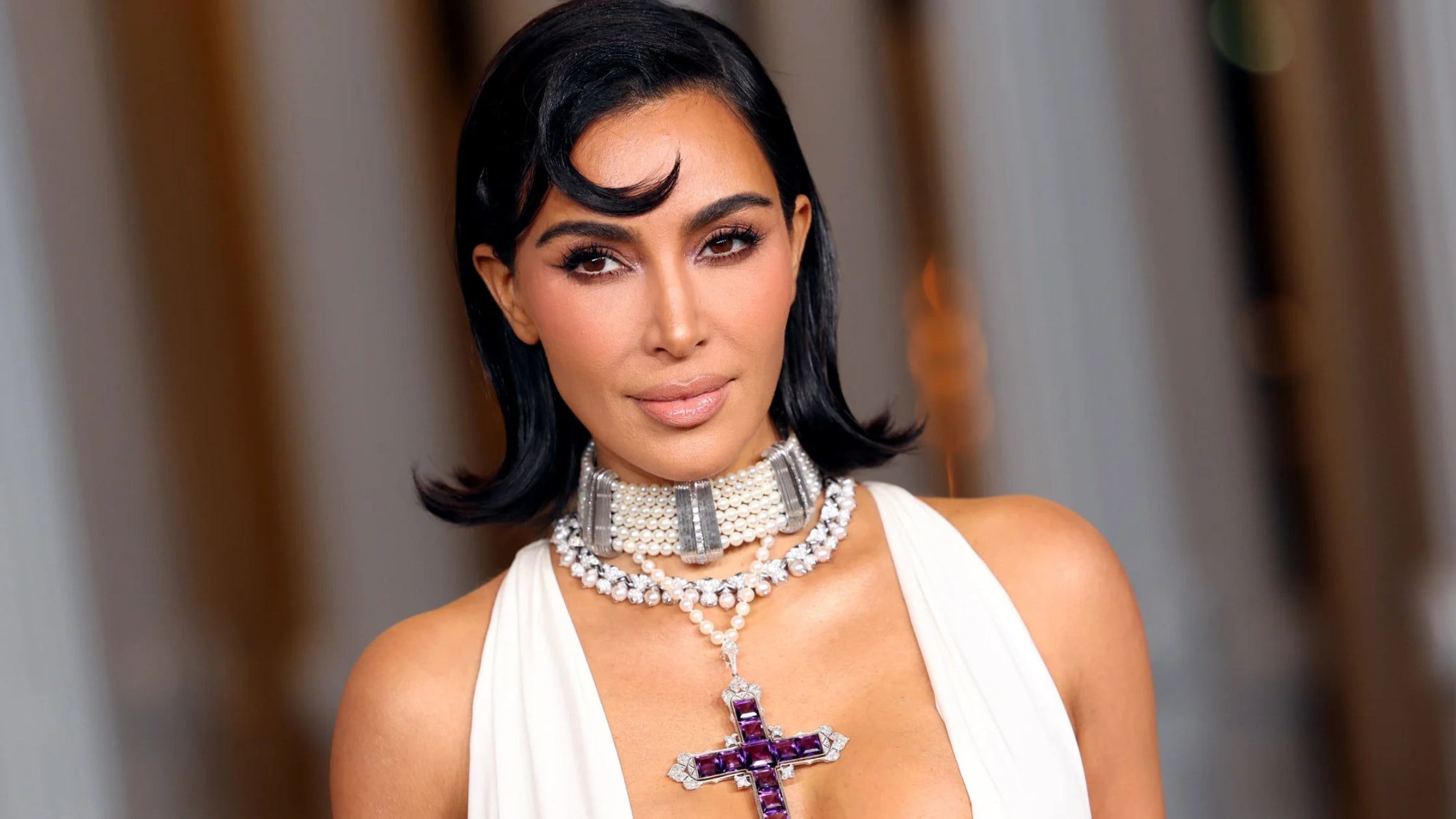 Kim Kardashian in a white gown wearing stacks on necklaces with an amethyst cross necklace once worn by the late Princess Diana.