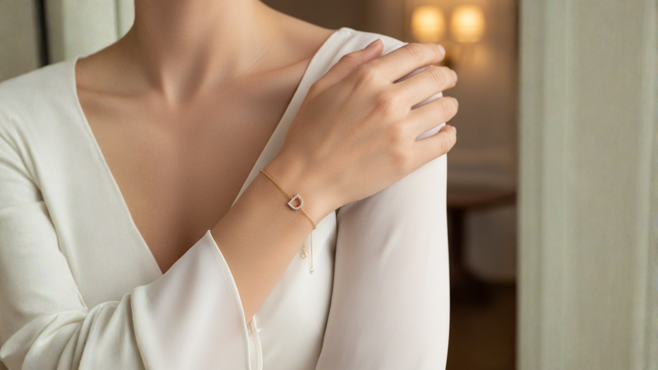 A women in white dress wearing a diamond initial bracelet in her right hand, placed over her shoulder. The initial is the letter D, in a 10K Yellow Gold Setting with Natural Diamonds